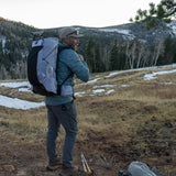 Side profile of hiker carrying Carbon Evo 50 backpack with trekking poles and full pack load