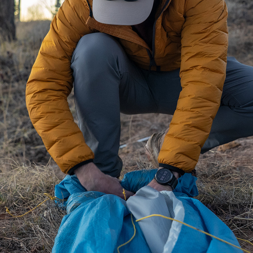 Backpacker packing ultralight trekking pole tent into stuff sack in the backcountry