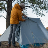 Backpacker adjusting ultralight trekking pole tent during setup in mountain campsite