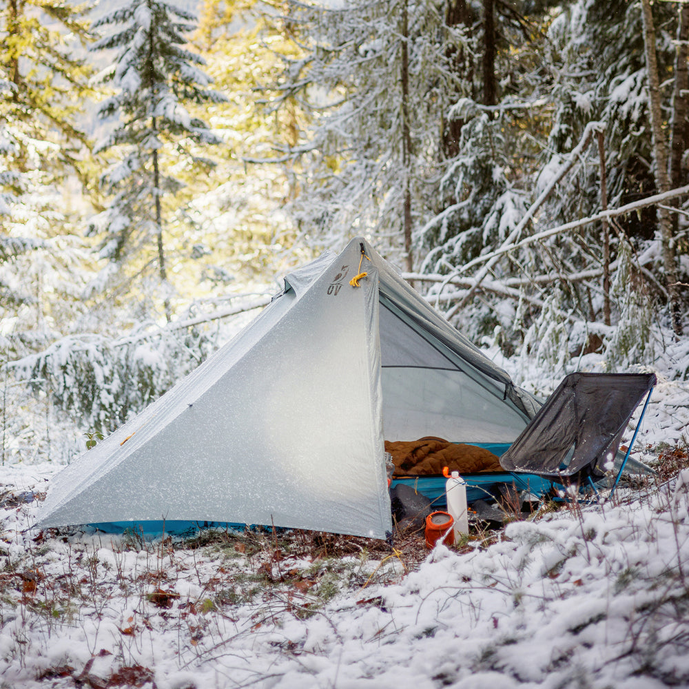 Tent pitched in a snowy forest with trees covered in snow.
