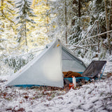Tent pitched in a snowy forest with trees covered in snow.
