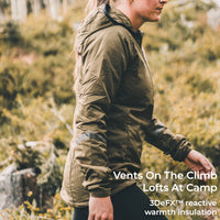 A woman wearing an olive green technical outdoor jacket is shown in profile walking through a grassy, rocky outdoor environment. White text overlay on the bottom right reads 'Vents On The Climb Lofts At Camp 3DeFX™ reactive warmth insulation'.