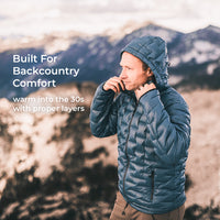 A man wearing a blue hooded puffer jacket stands outdoors in front of a mountain landscape, with text on the left reading 'Built For Backcountry Comfort' and 'warm into the 30s with proper layers'.