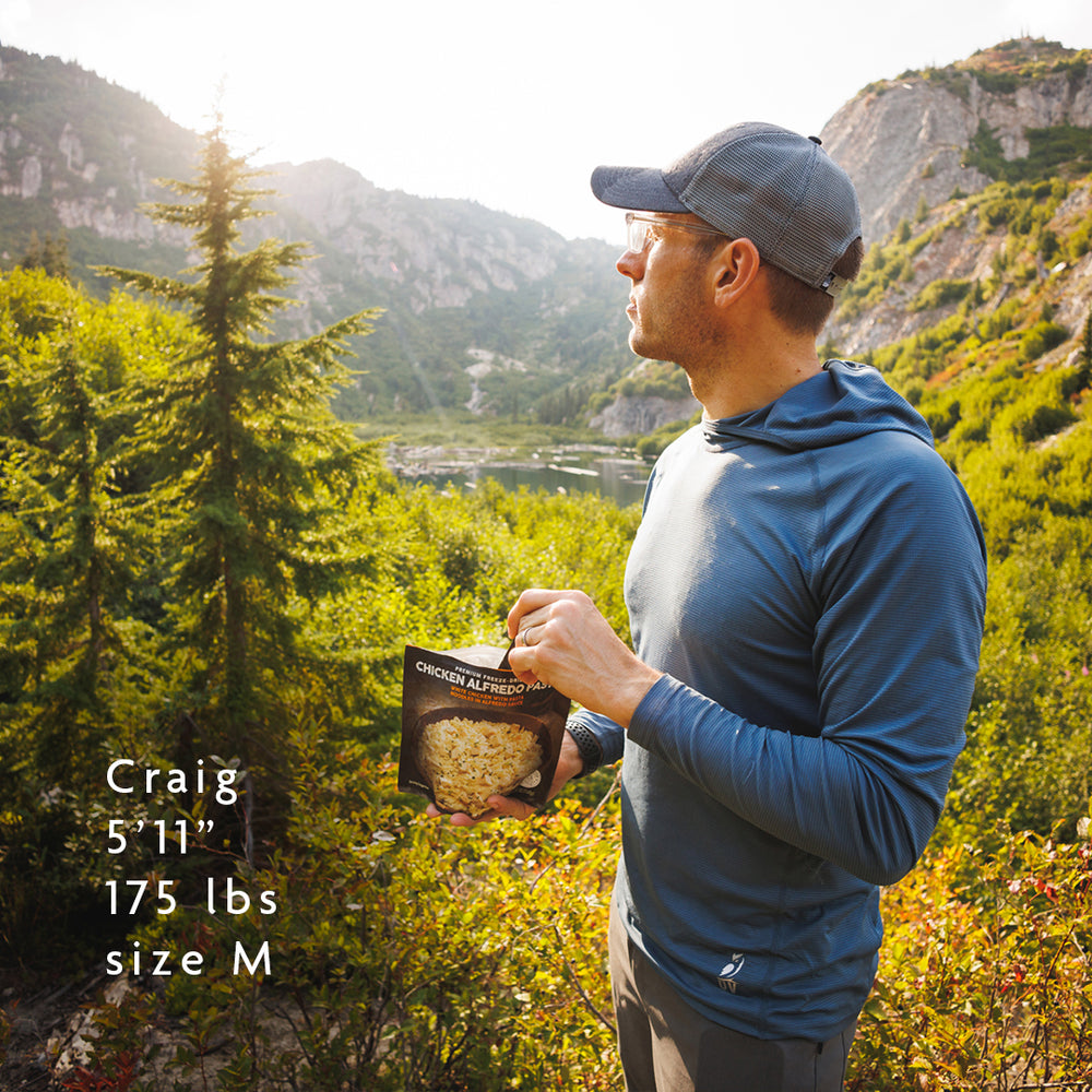man wearing blue lightweight sun hoodie while eating a backpacking meal