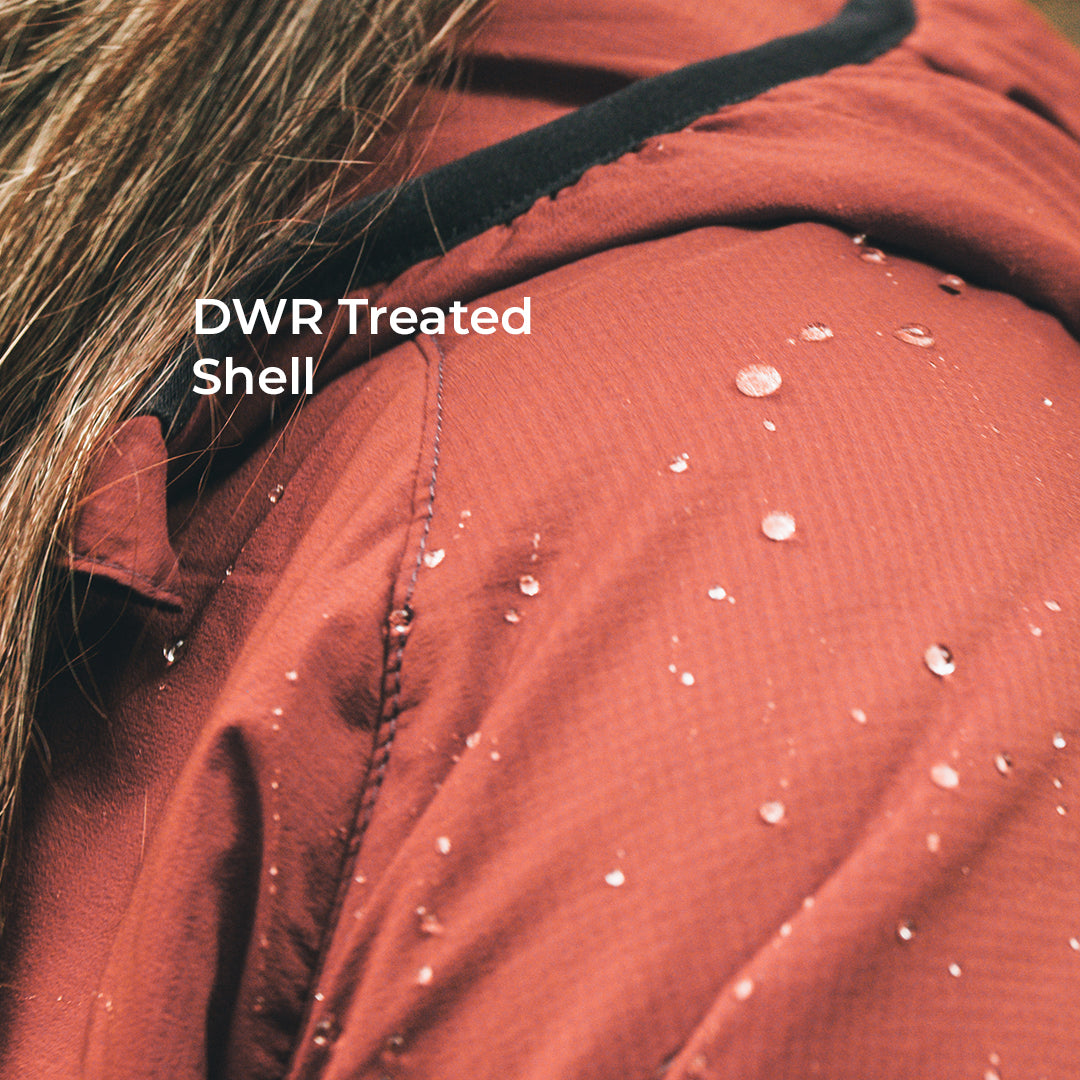 Close-up of a terracotta-colored waterproof jacket with water droplets on the surface, featuring a black collar trim and white text overlay that reads 'DWR Treated Shell'.