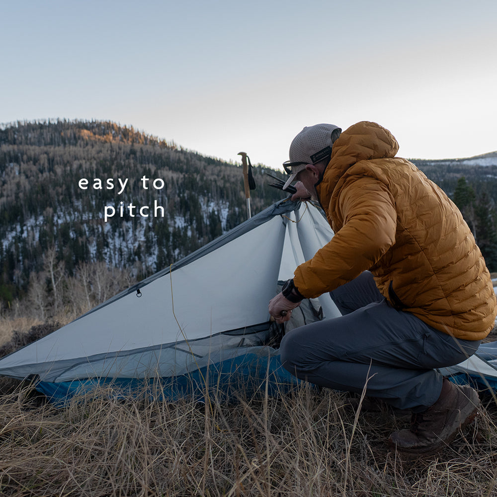 Backpacker setting up ultralight trekking pole tent in mountain terrain