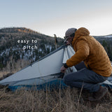 Backpacker setting up ultralight trekking pole tent in mountain terrain
