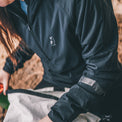 A close-up of a person wearing a dark navy waterproof jacket sitting outdoors next to a light-colored bag.