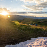 distant view of 4 trekking pole tents pitched in high mountain basin as sun rises