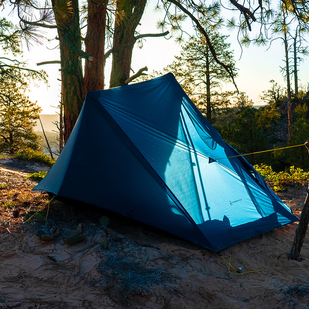 rear view of blue 1 person trekking pole tent as sun shines & illuminates the fabric from the other side