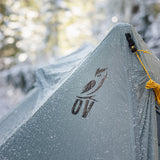 trekking pole tent covered in frost in a snowy forest setting