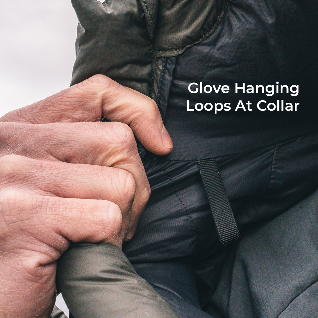 A close-up of a person's gloved hand pulling a black hanging loop at the collar of a dark insulated jacket, with white text overlay reading 'Glove Hanging Loops At Collar'.