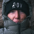 Close-up of a person wearing a black knit beanie along with a dark puffer jacket with the hood up.