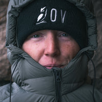 Close-up of a person wearing a black knit beanie along with a dark puffer jacket with the hood up.