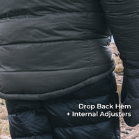 Close-up of a black puffer jacket worn outdoors, showing the lower back and hip area with text reading 'Drop Back Hem + Internal Adjusters'.