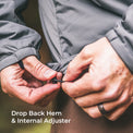 Close-up of a person's hands adjusting the hem of a gray jacket, demonstrating the drop back hem and internal adjuster feature. White text at the bottom reads 'Drop Back Hem & Internal Adjuster'.