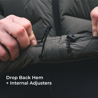 Close-up of a person's hands adjusting the hem of a dark olive green puffer jacket using internal drawstring toggles, with text overlay reading 'Drop Back Hem + Internal Adjusters'.
