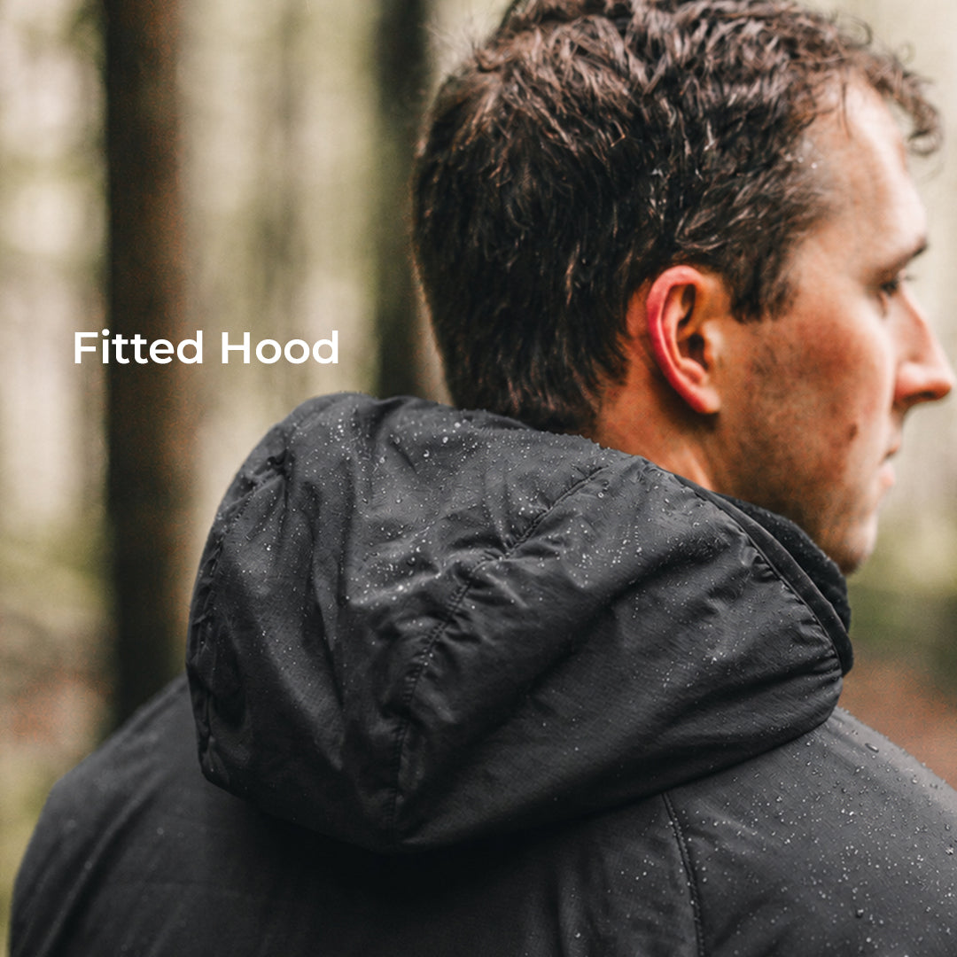 A man shown from the side and back wearing a black fitted hooded jacket outdoors in a blurred forest setting. The text 'Fitted Hood' appears on the left side.