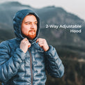 A man wearing a blue insulated puffer jacket with a hood, shown outdoors against a blurred mountain background. He is adjusting the hood, and white text on the right reads '2-Way Adjustable Hood.