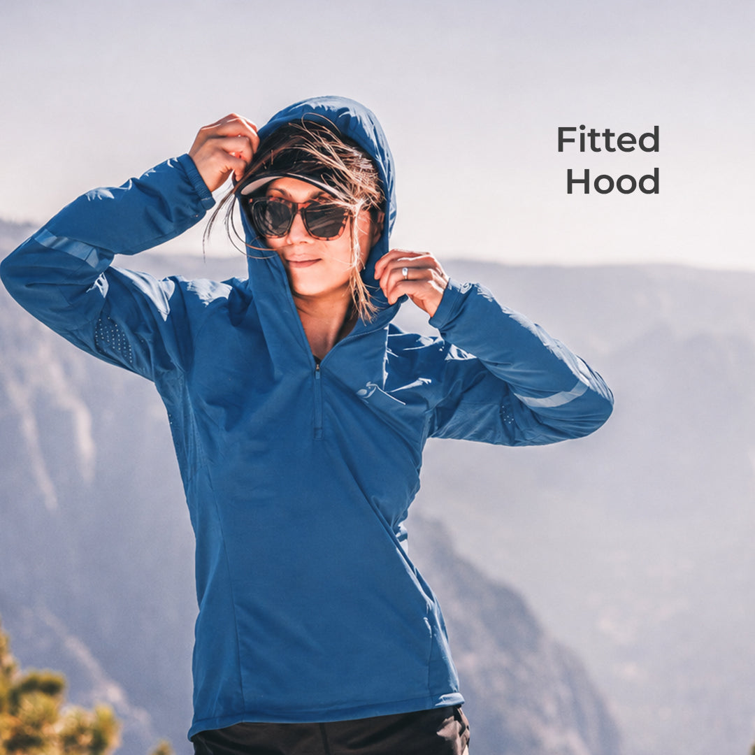 A woman wearing a fitted blue hooded athletic jacket stands outdoors against a blurred mountain background, adjusting the hood. The text 'Fitted Hood' appears in the upper right.