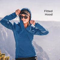 A woman wearing a fitted blue hooded athletic jacket stands outdoors against a blurred mountain background, adjusting the hood. The text 'Fitted Hood' appears in the upper right.