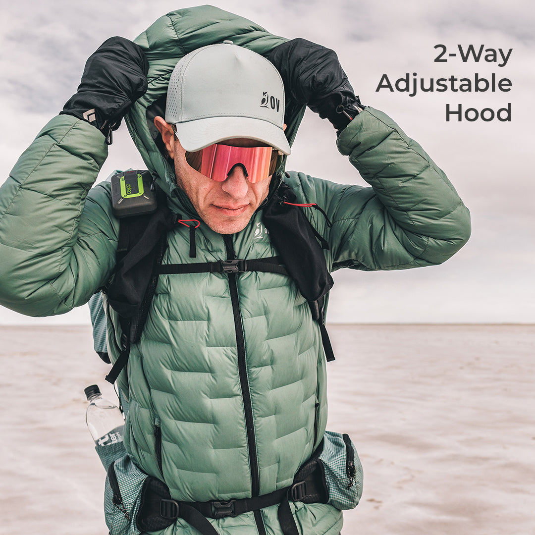 A man wearing a sage green puffer jacket with an adjustable hood, black gloves, and reflective sunglasses, adjusting the hood. The text '2-Way Adjustable Hood' is visible in the top right corner.