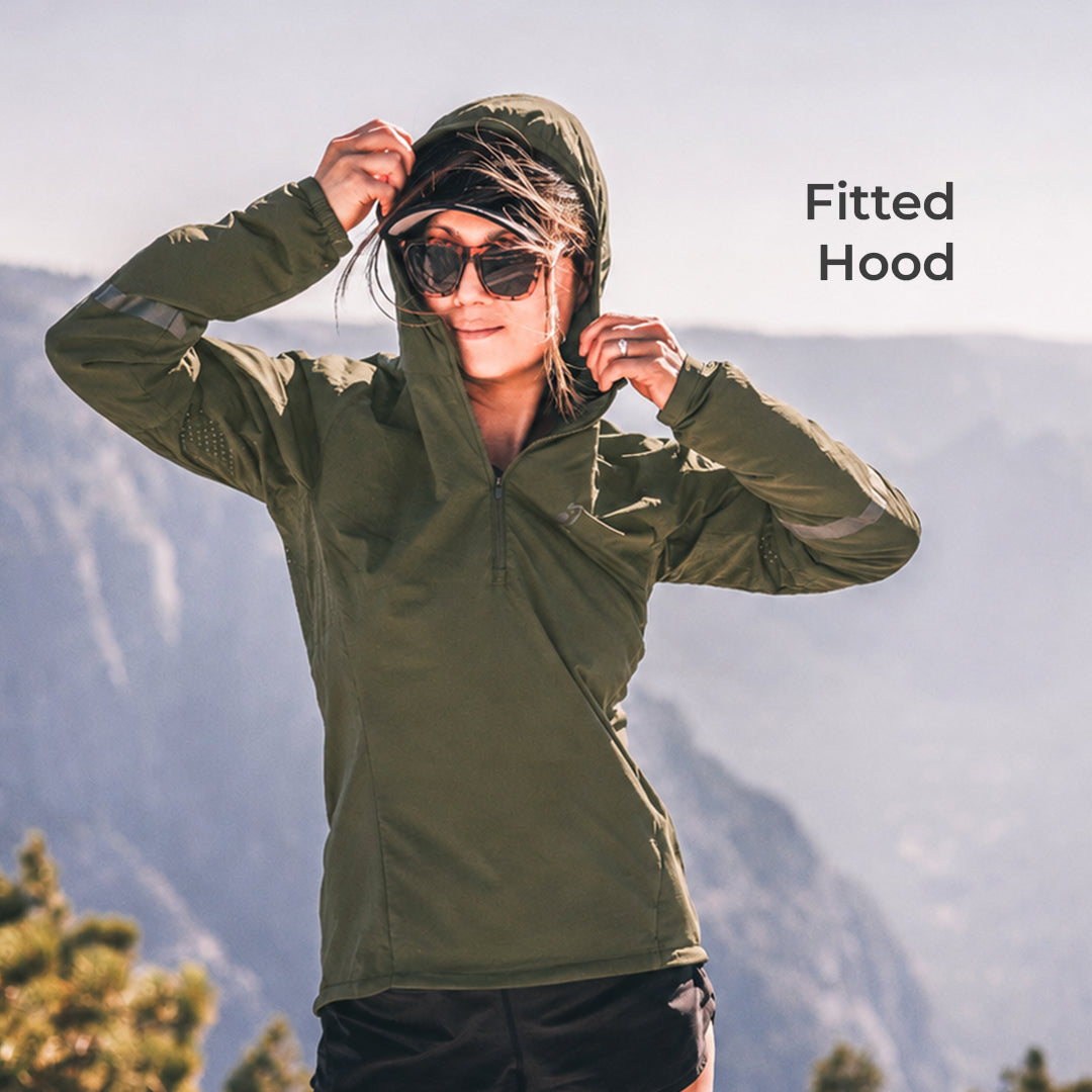 A woman wearing an olive green fitted hooded athletic jacket stands outdoors against a blurred mountain background, adjusting the hood with both hands. The text 'Fitted Hood' appears in the upper right.