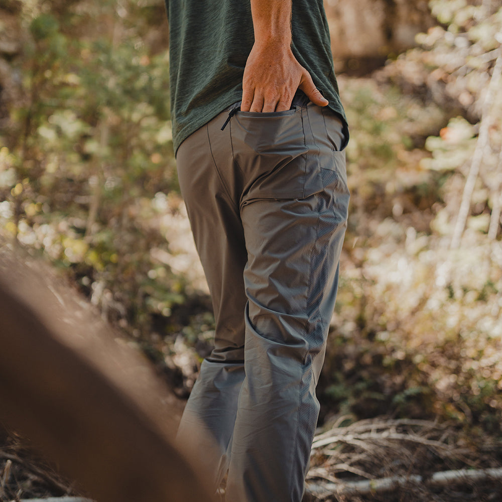 wide rear view of man sliding item into rear pocket of ultralight hiking pants