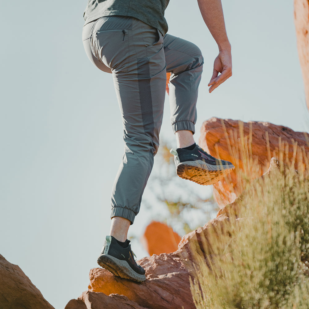 hiker climbing steep rocky hillside wearing flexible trail pants