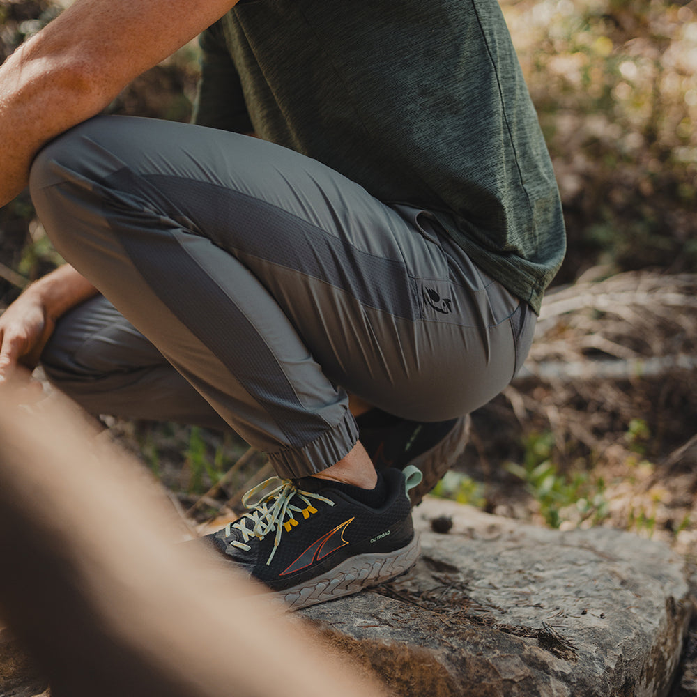 side view of hiker crouched on a rock while wearing gray hiking joggers