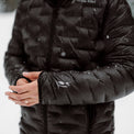 Close-up of a person wearing a black Outdoor Vitals insulated jacket in the snow, showing thumb loop cuffs with the brand’s logo on the sleeve.