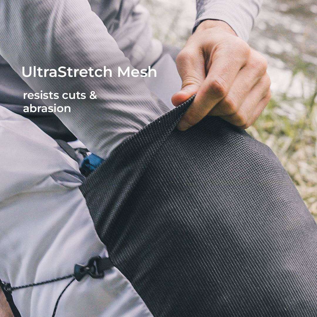 close view of hiker pulling gear from the large mesh pocketing on the exterior of a technical backpack. Text callout says, "UltraStretch Mesh - resists cuts & abrasion."