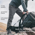 side view of man wearing gray lightweight mountain pants on a peak while picking up a backpack