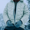 Person wearing a light gray Outdoor Vitals insulated jacket in snowy conditions, shown mid-zip with frosted gloves and visible snowflakes on the fabric.