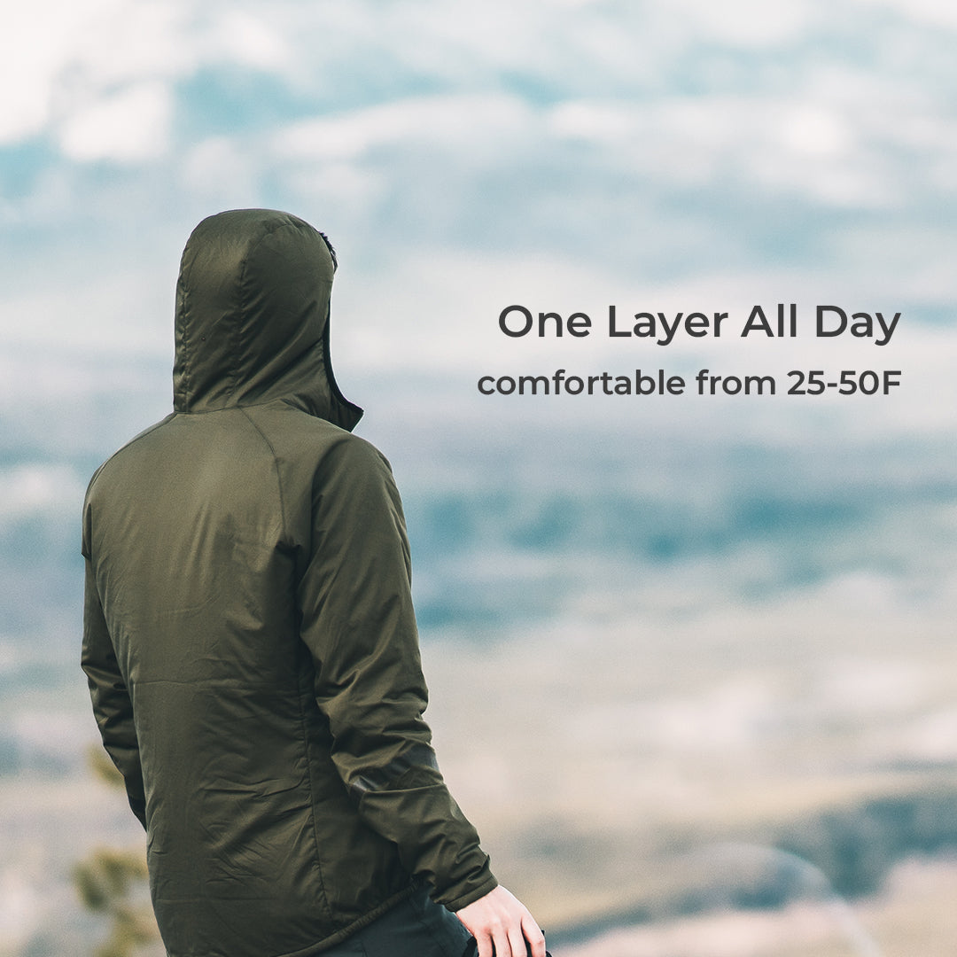 A person wearing an olive green hooded jacket stands with their back to the camera, looking out over a hazy mountain landscape. Text on the right reads 'One Layer All Day' and 'comfortable from 25-50F'.