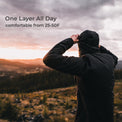 A person wearing a black hooded jacket stands outdoors on a mountain landscape at sunset, with text in the upper left reading 'One Layer All Day' and 'comfortable from 25-50F'.