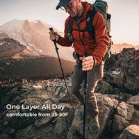 A man hiking on rocky mountainside wearing a one-layer jacket, brown pants, and a green backpack, holding trekking poles. Text overlay reads 'One Layer All Day comfortable from 25-50F'.
