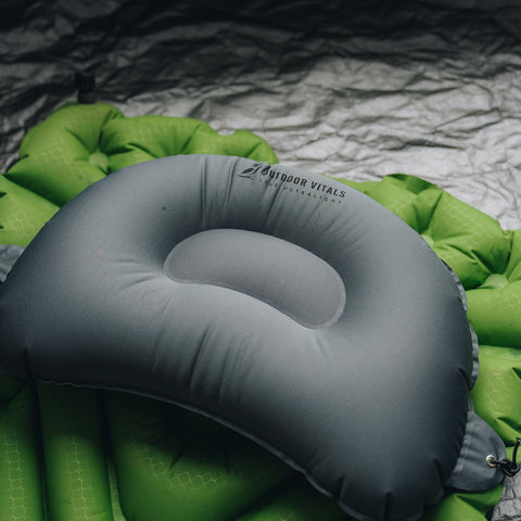 Outdoor Vitals ultralight inflatable pillow secured on top of a green sleeping pad, ready for use while camping.