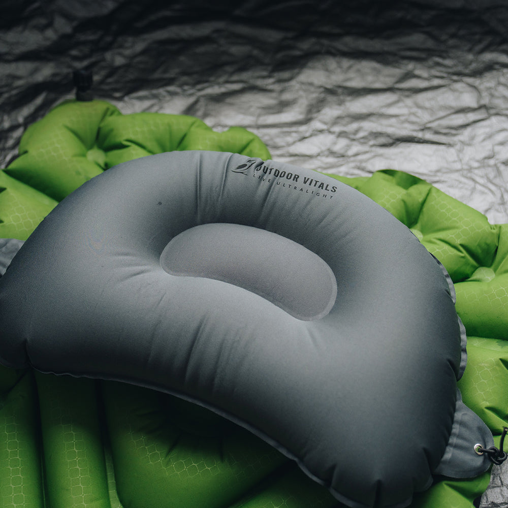 Outdoor Vitals ultralight inflatable pillow secured on top of a green sleeping pad, ready for use while camping.