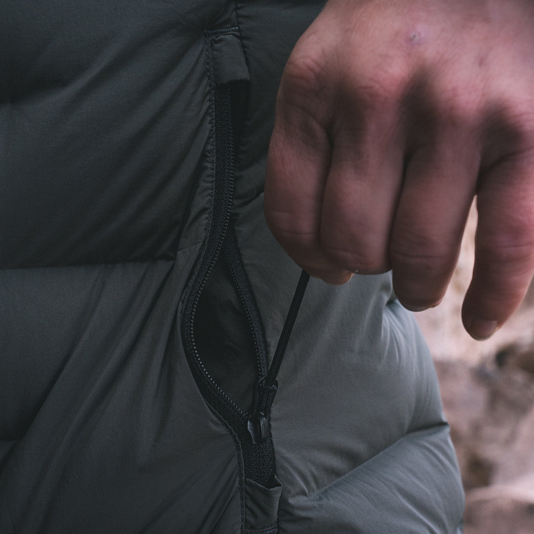 Close-up of a person's hand unzipping the side pocket of a dark gray puffer jacket.