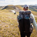 Rear view of a hiker carrying the Outdoor Vitals Shadowlight backpack loaded with gear in mesh front and side pockets, trekking across an open alpine landscape.
