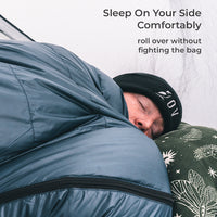 A person sleeping comfortably inside a blue sleeping bag, rolled over to show the side zipper.