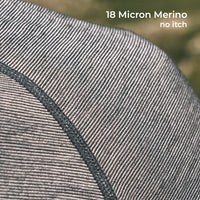 Close-up of a fine knit fabric texture in a gray and off-white merino weave, with a dark gray seam and white text reading '18 Micron Merino no itch' in the top right.