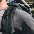 Close-up of a person wearing a backpack over a wool shirt outdoors, with the text 'Naturally Odor Resistant' in the top right corner.