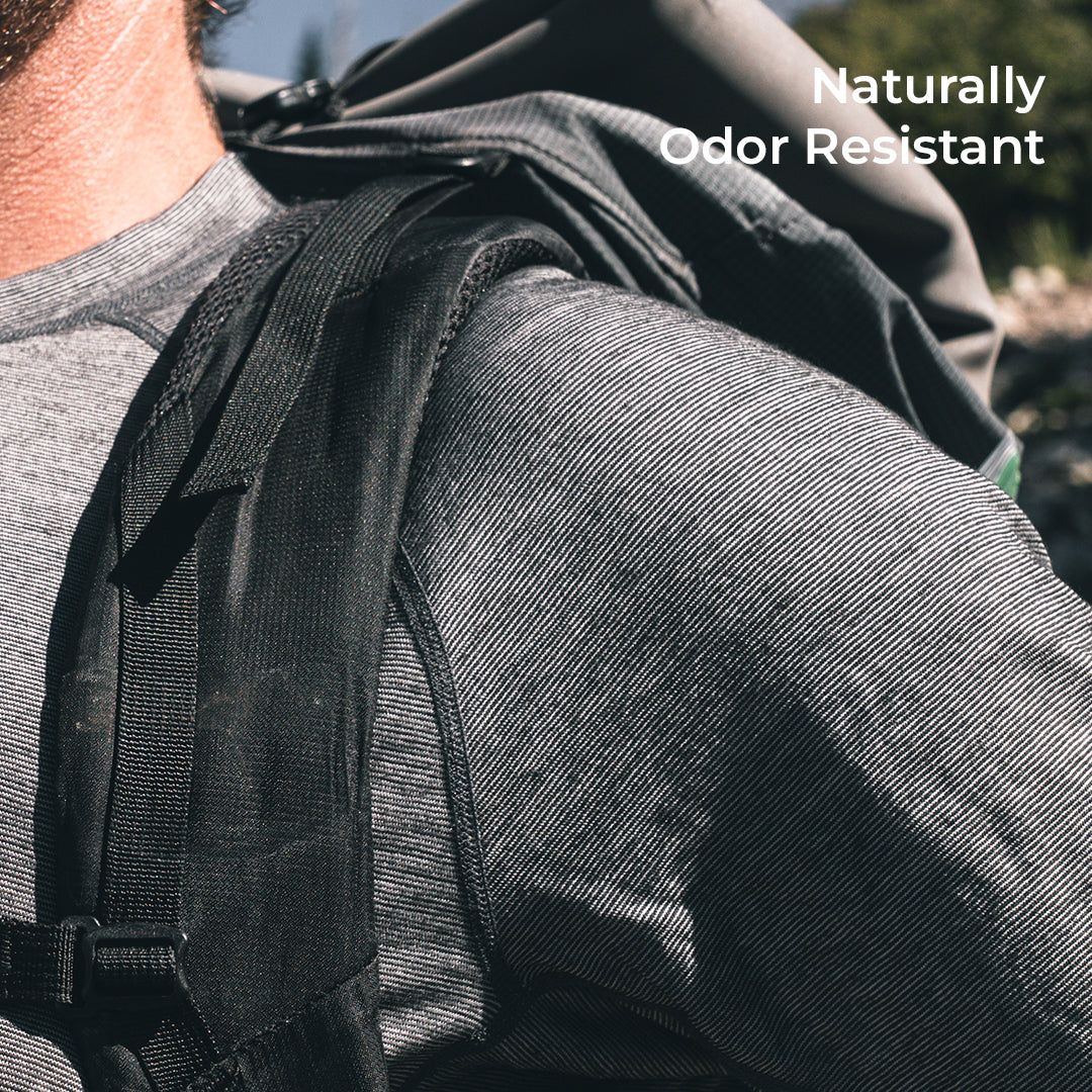 Close-up of a person wearing a backpack over a wool shirt outdoors, with the text 'Naturally Odor Resistant' in the top right corner.