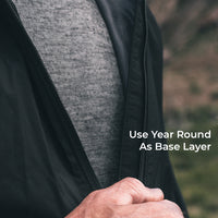 Close-up of a person wearing a black lightweight zip-front layer over a wool base layer, with a blurred outdoor background and the text 'Use Year Round As Base Layer' on the right.