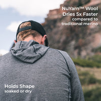 A man viewed from behind wearing a heather gray hooded top outdoors in front of a rocky cliff, with white text overlays about NuYarn Wool drying faster and holding shape.