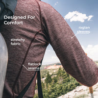 A close-up of a person outdoors wearing a textured merino wool long-sleeve top, with text callouts highlighting stretchy fabric, flatlock seams, and raglan sleeves against a scenic mountain background.