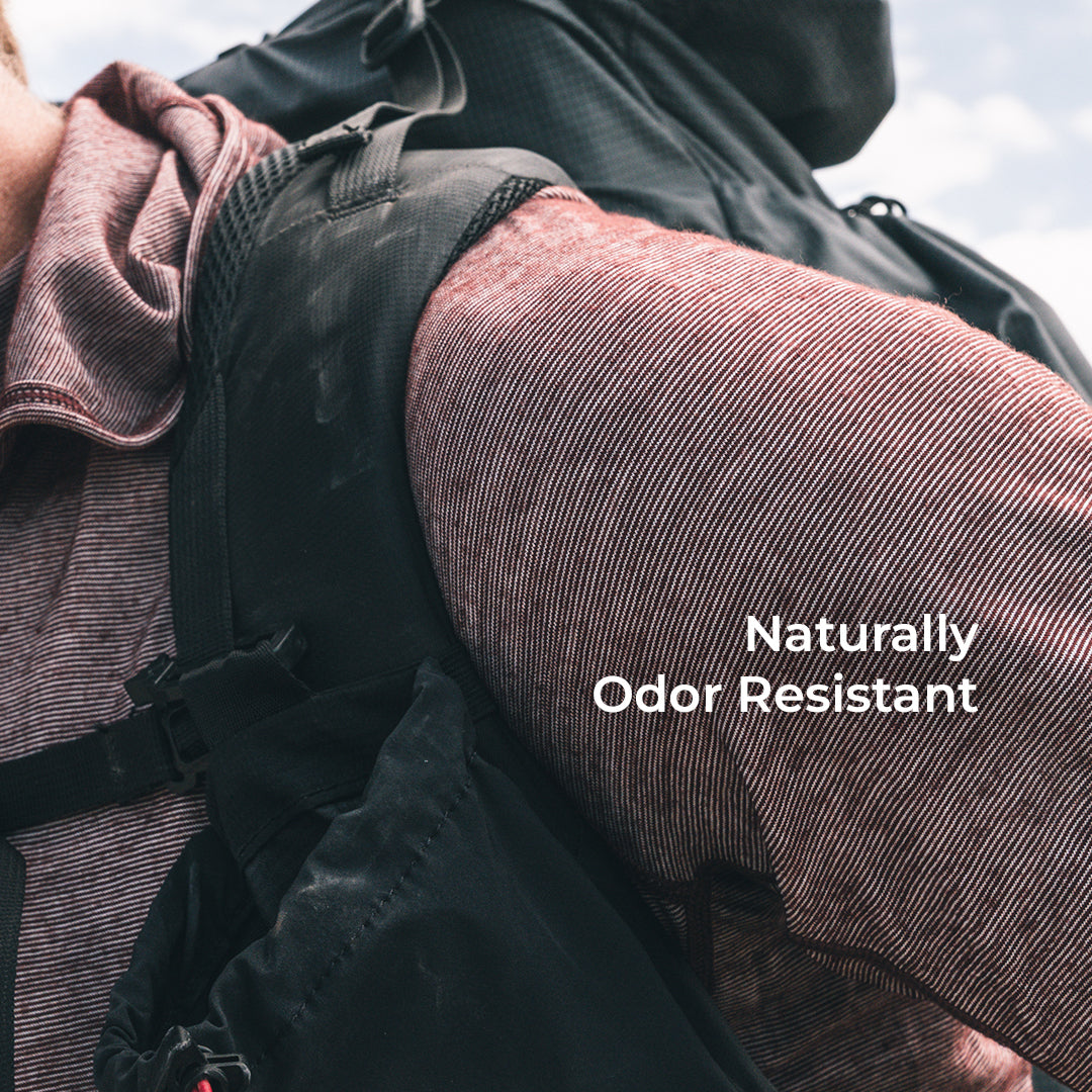 Close-up of a person wearing a backpack and a wool long-sleeve top, with the text 'Naturally Odor Resistant' overlaid on the right side.