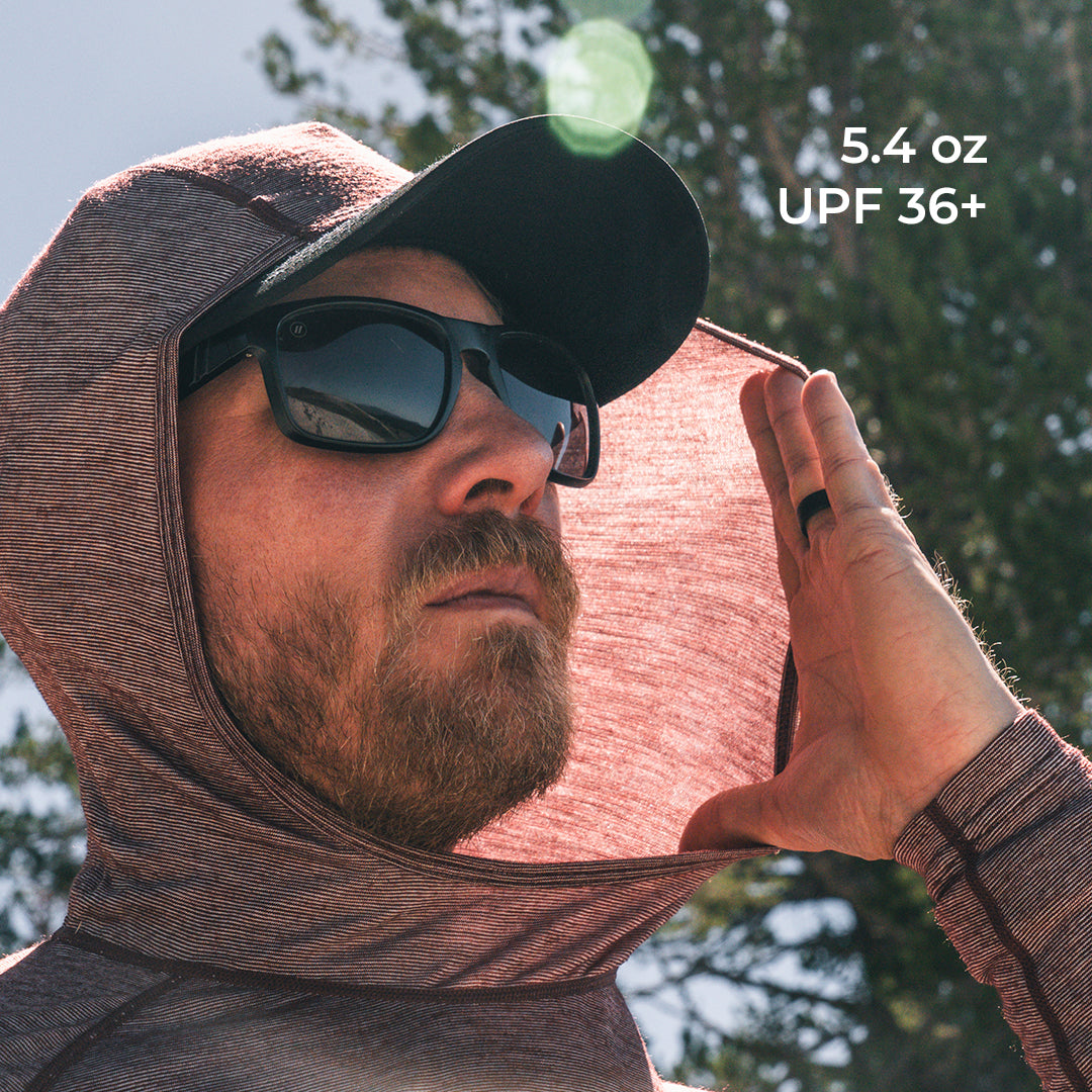 A man outdoors wearing a hooded long-sleeve shirt demonstrating how the fabric blocks the sun